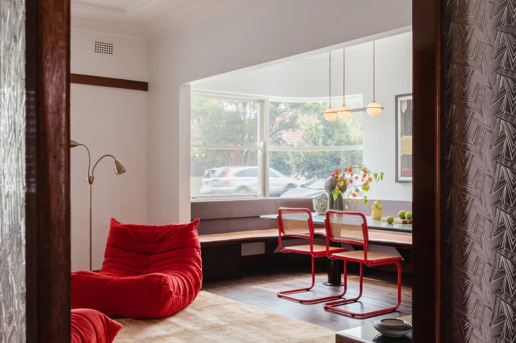 Sunlit dining nook with two red cantilever chairs and a red lounge chair in an otherwise neutral room.