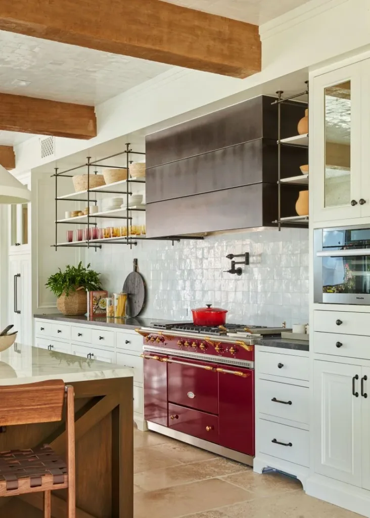 Bright white kitchen with a deep red range and a red pot on the stovetop, open shelves, and warm wood details.